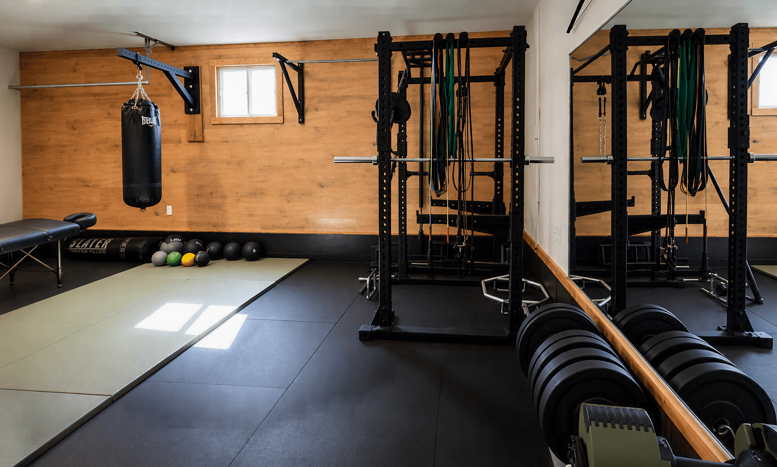 Modern home gym with spin bikes, a treadmill, elliptical machine, punching bag, and weight rack, with wood paneling and mirrored walls